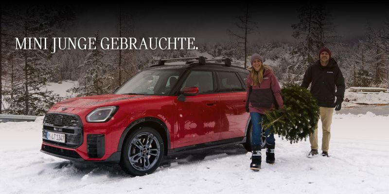 Vergessen Sie Ihren alten Schlitten. Jetzt Traum MINI entdecken. Ein roter MINI, eine Frau und ein Mann mit einem Weihnachtsbaum.